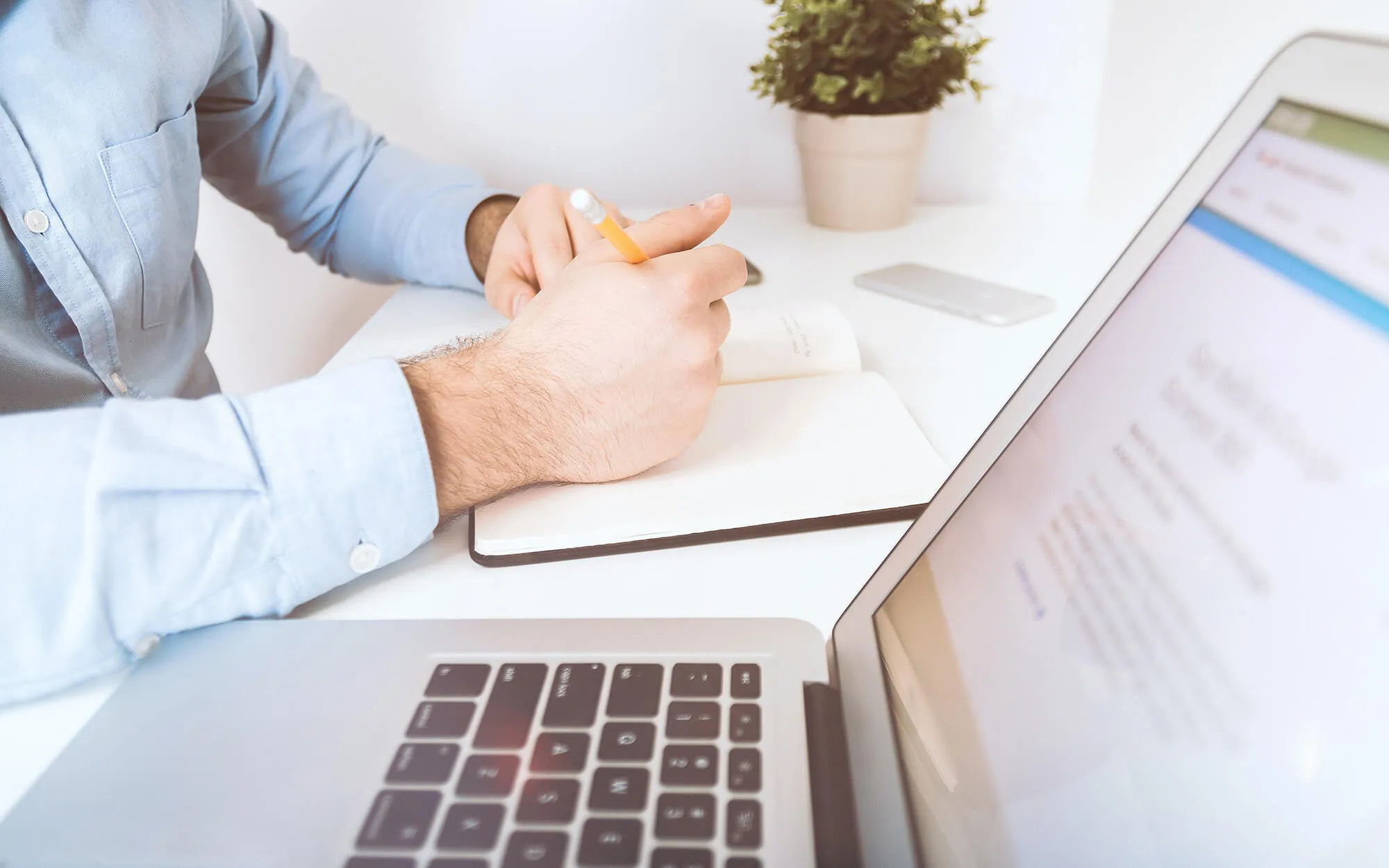 Laptop und der Ausschnitt einer Hand, die etwas in ein Notizbuch einträgt